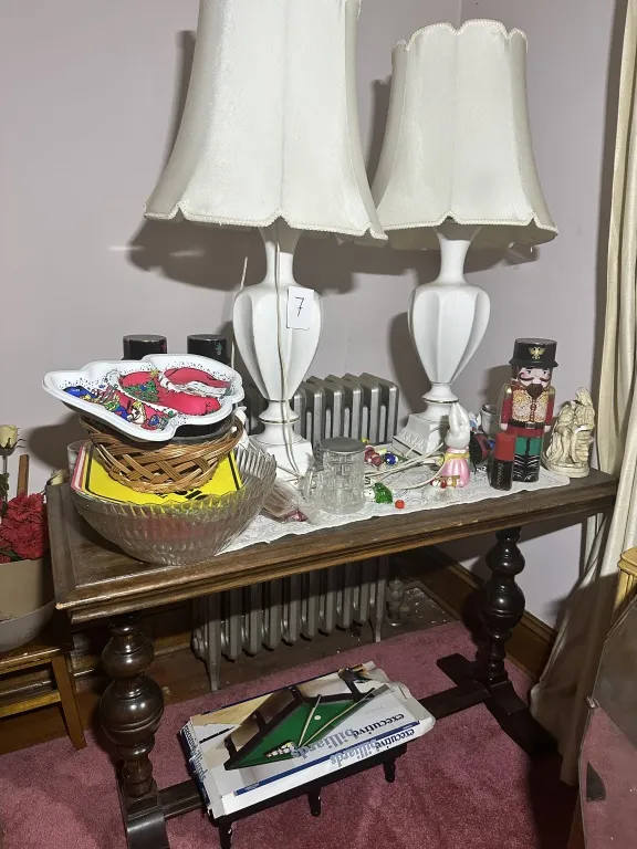 Table With Lamps & Contents wood table with turned legs, pair of white table lamps, glass bowl, basket, holiday plate, nutcracker, small figurines, and assorted contents as shown from auction in Clifford , Pennsylvania